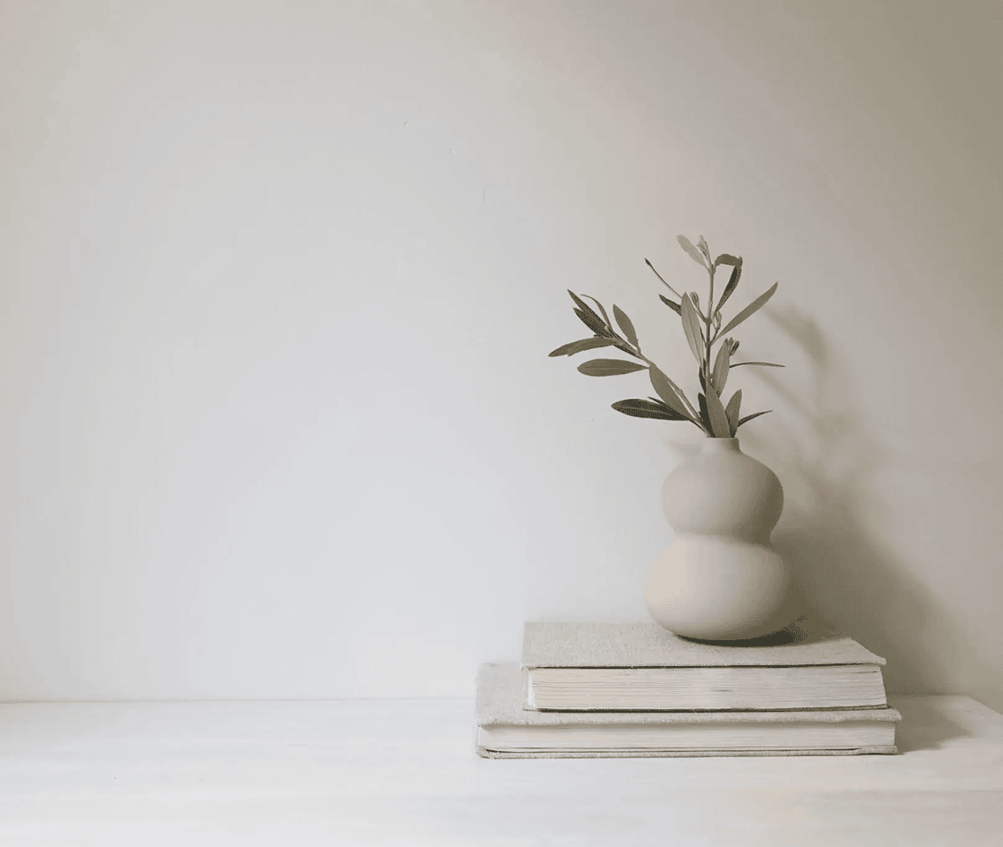 White vase sitting atop a stack of books on a table, with a wall in the background